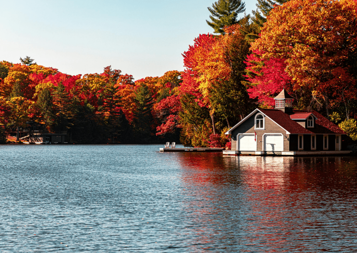Maison en bois au bord d’un lac, entourée d’arbres flamboyants rouges et orangés, typique d’un voyage automnal au Canada