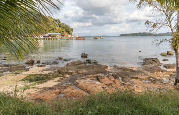 Petite plage avec rochers, eau calme et bateaux de pêche, entourée de végétation tropicale.