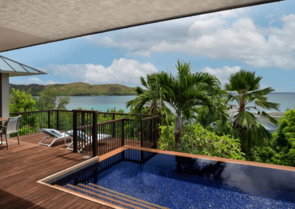Villa luxueuse du Raffles Seychelles avec piscine privée, terrasse en bois et vue panoramique sur l’océan Indien, entourée de palmiers et de végétation tropicale.