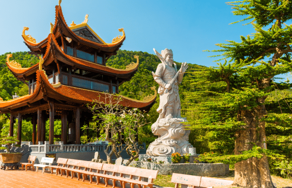 Temple traditionnel vietnamien avec une grande statue blanche devant une colline verdoyante.
