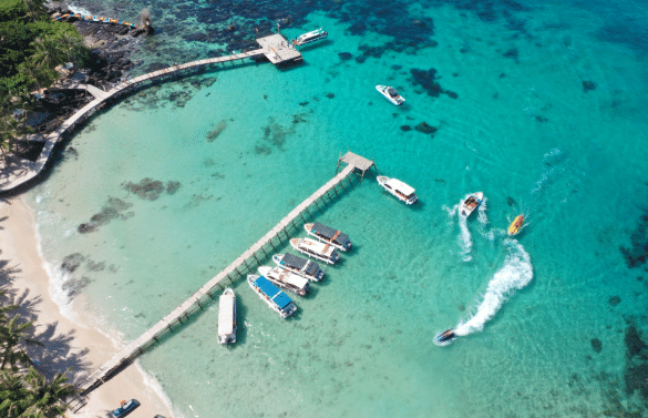 Vue aérienne d’une plage tropicale à Phú Quốc avec pontons, bateaux et eau turquoise.