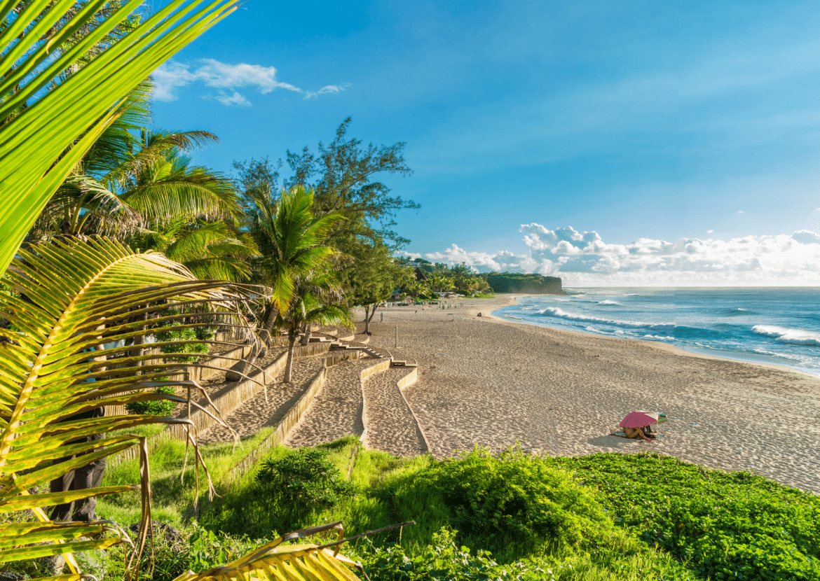 Vue panoramique d’une plage bordée de palmiers à La Réunion, sable doré et lagon bleu sous un ciel ensoleillé — destination idéale pour les vacances de la Toussaint.
