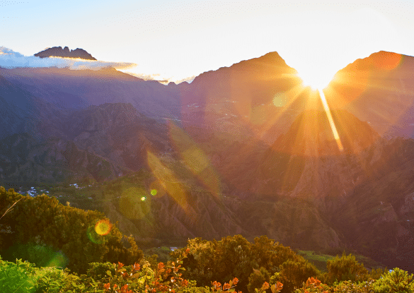 Lever du soleil sur les montagnes du cirque de Mafate à La Réunion, baignant les sommets verdoyants de lumière dorée et offrant une vue spectaculaire sur l’île.