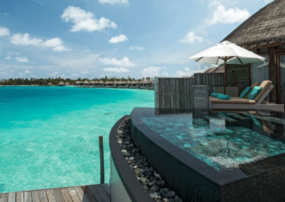 Vue sur une villa sur pilotis avec piscine privée au Constance Halaveli Maldives, donnant sur un lagon turquoise et des bungalows bordant l’horizon sous un ciel ensoleillé.