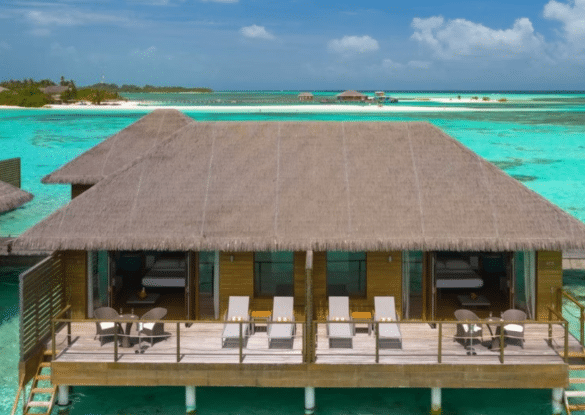 Villa sur pilotis au Cocoon Maldives avec terrasse privée, transats et vue imprenable sur le lagon turquoise et les plages de sable blanc de l’atoll.