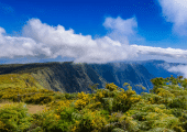 Vue du cirque de Mafate à La Réunion, avec falaises verdoyantes, nuages bas et ciel bleu lumineux.