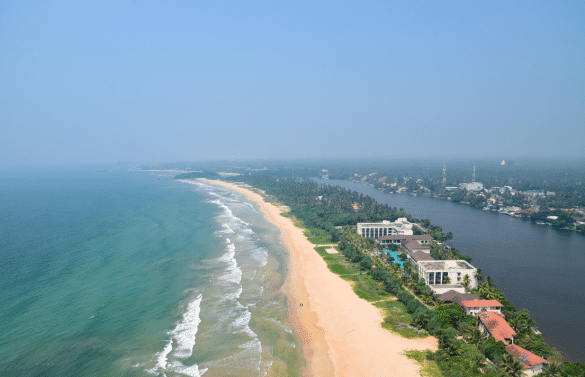 Vue aérienne de Bentota avec longue plage sable doré, océan et lagune entourée de végétation tropicale.