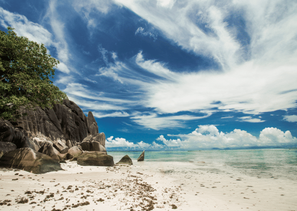 Plage paradisiaque de l’île de Praslin aux Seychelles avec sable blanc, rochers de granit sculptés par le vent et lagon turquoise sous un ciel bleu éclatant.