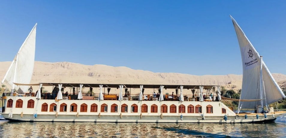 Dahabieh traditionnelle naviguant sur le Nil – Égypte Dahabieh à voiles naviguant sur le Nil, avec le désert et un ciel bleu en arrière-plan.