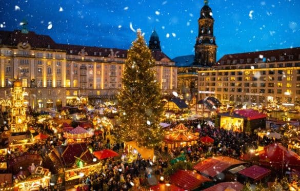 Marché de Noël traditionnel à Dresde en Allemagne avec un grand sapin illuminé, des chalets décorés et la neige qui tombe sur la vieille ville.