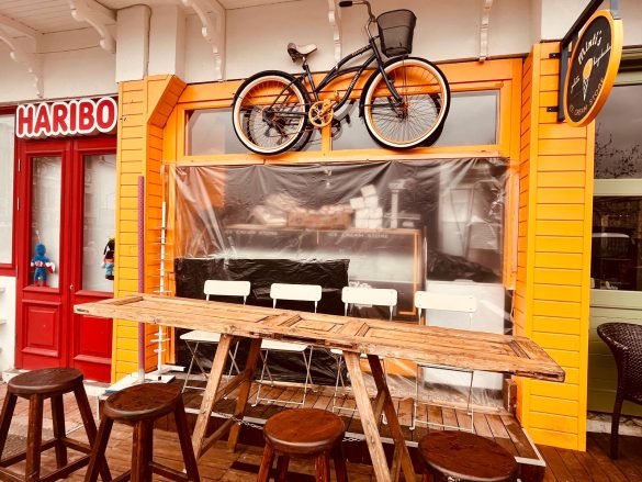 Façade orange d’un café à Madère avec un vélo noir suspendu au-dessus de l’entrée et des tabourets en bois en terrasse.