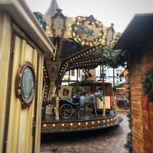 Carrousel ancien illuminé sur le marché de Noël d’Obernai en Alsace, entouré de chalets et de décorations festives.