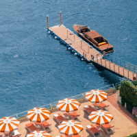 Grand Hotel Tremezzo au lac de Côme : hôtel de luxe avec plage privée et piscine flottante Ponton privé du Grand Hotel Tremezzo sur le lac de Côme avec bateau en bois et parasols orange emblématiques au bord de l’eau