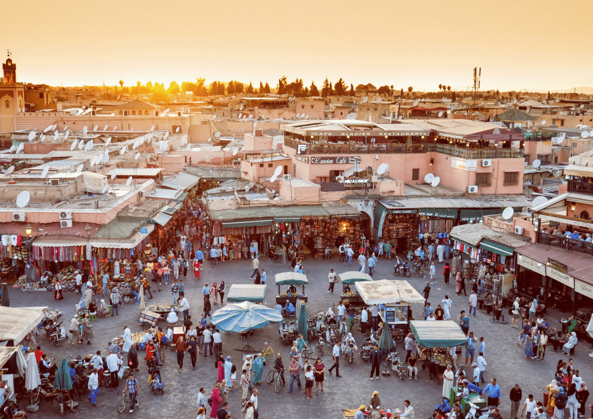 Vue panoramique de la place Jemaa el-Fna à Marrakech au coucher du soleil, avec les souks animés, les étals de marché et les toits de la médina marocaine.