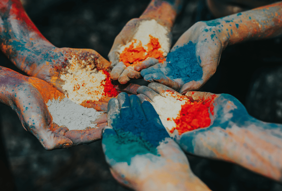 Mains couvertes de pigments colorés symbolisant la diversité culturelle, le partage et la richesse des voyages à travers le monde.