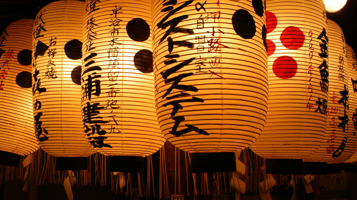 Lanternes japonaises traditionnelles illuminées dans une rue au Japon, symbole de la culture japonaise et illustration d'un guide de voyage avec 30 conseils pratiques avant de partir au Japon.